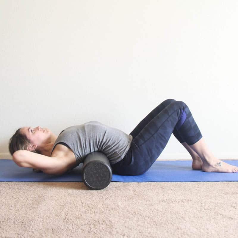 Person performing upper back foam rolling exercise on mat.